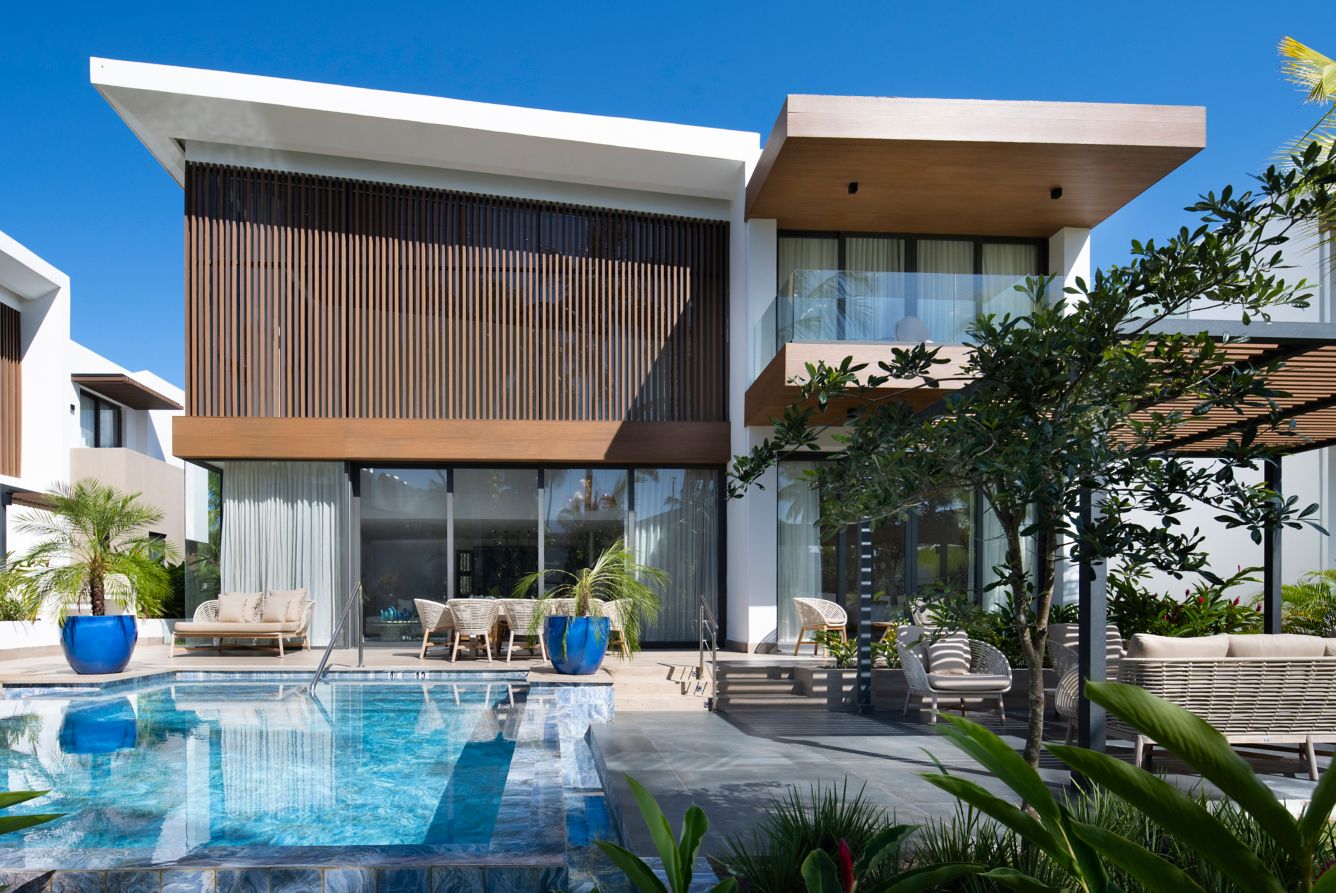 Modern luxury resort villa with a private swimming pool, patio seating, and lush tropical landscaping.