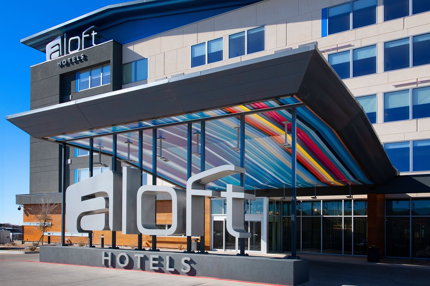 Exterior view of an Aloft Hotels entrance featuring a colorful striped canopy and modern signage.