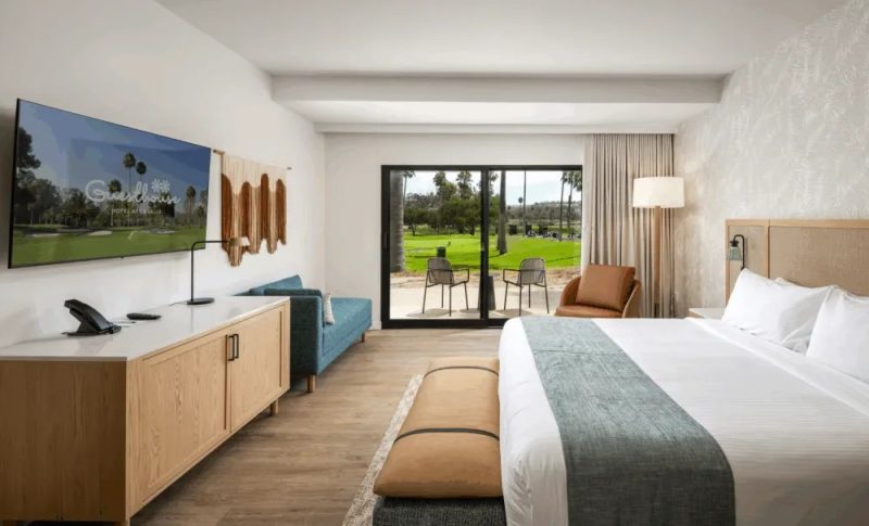 Accessible king hotel suite with wooden furniture, TV console, and sliding doors opening to a golf course patio.