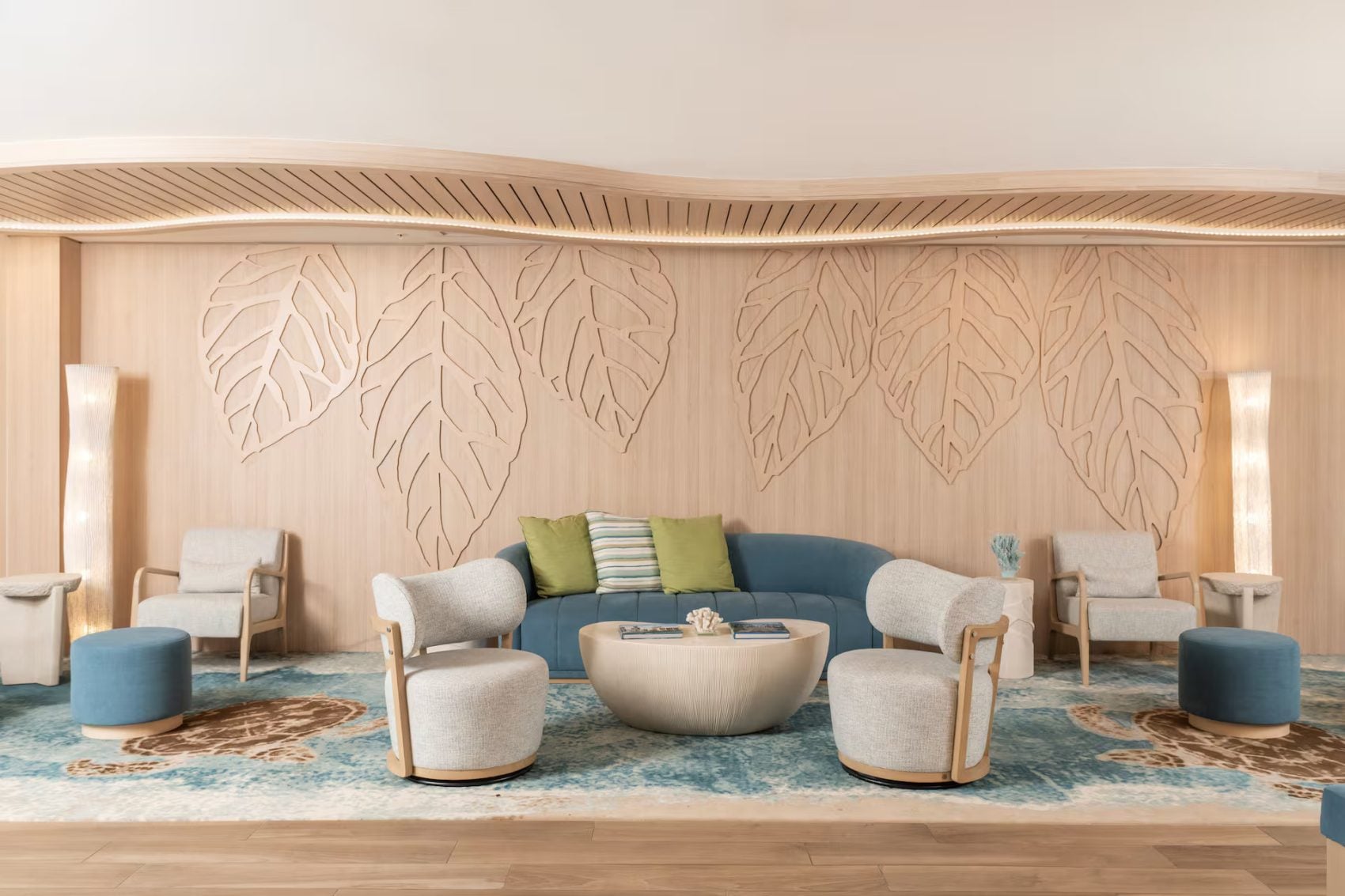 Modern hotel lounge area with blue and white armchairs, leaf-carved wall panel, and blue patterned rug at Hampton St. Thomas.