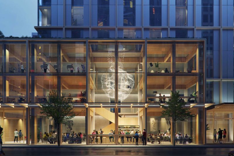 Modern multi-story hotel exterior with glass facade, illuminated multi-level lobby, and large glowing light fixture.