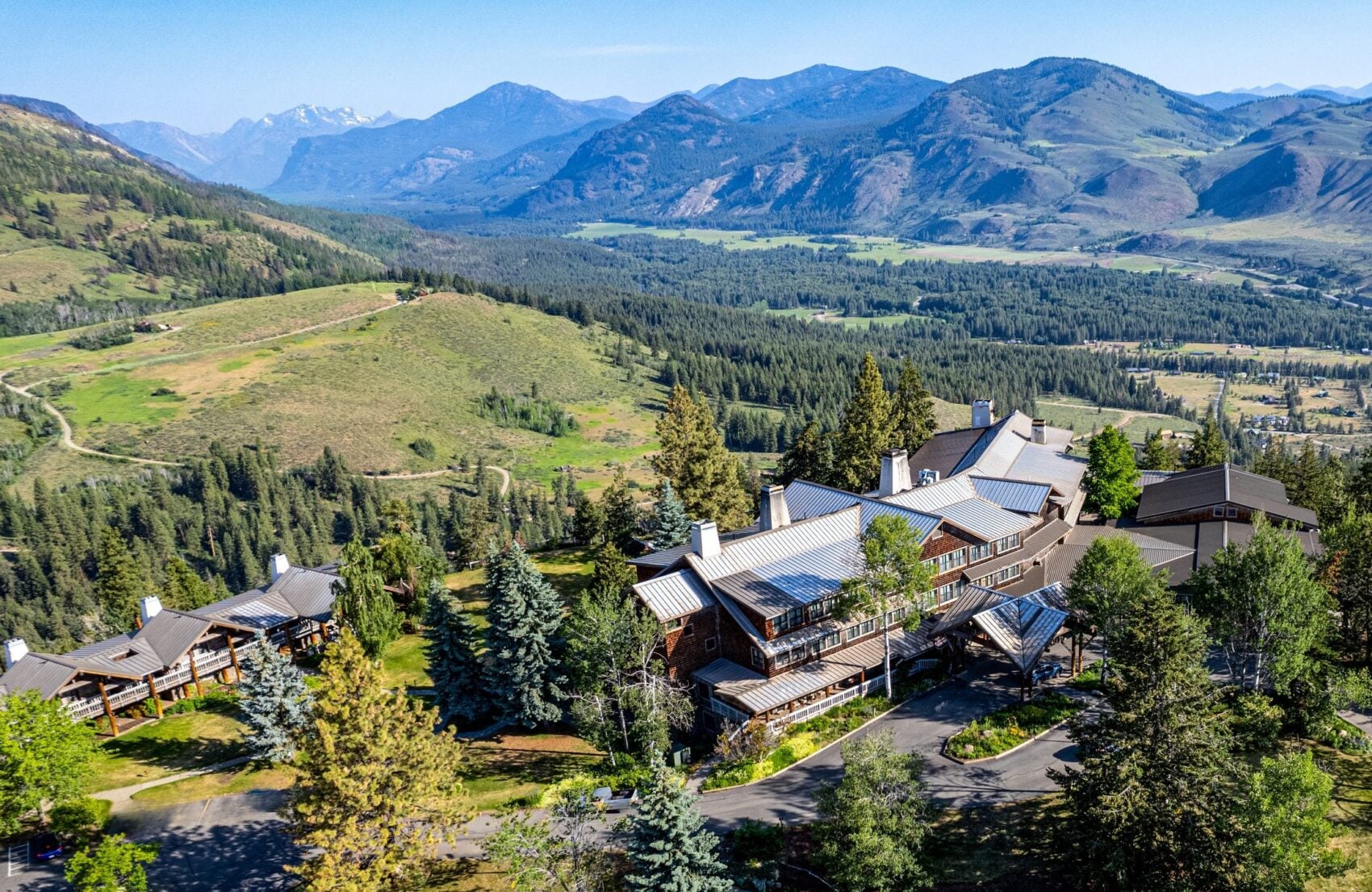 Aerial view of a mountain lodge among pines with valleys and peaks beyond