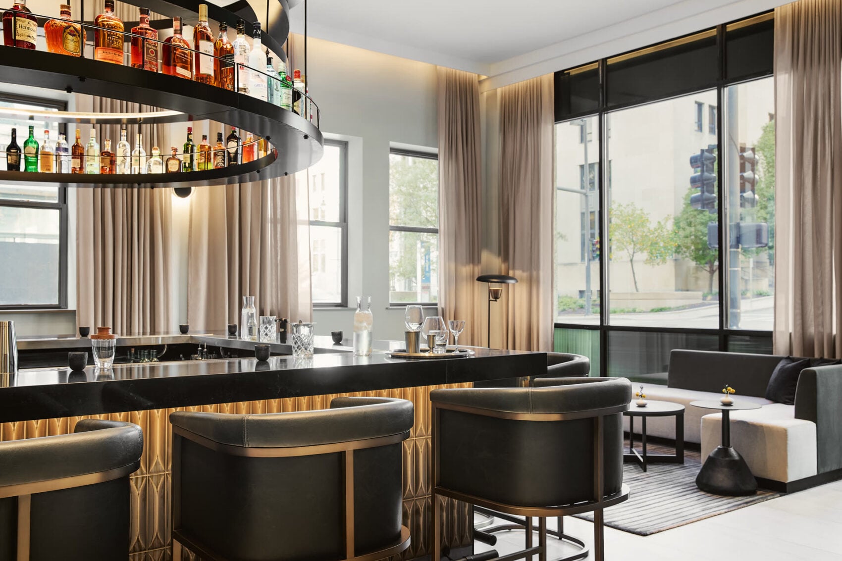 Hotel bar with a suspended bottle display, leather stools and tall windows