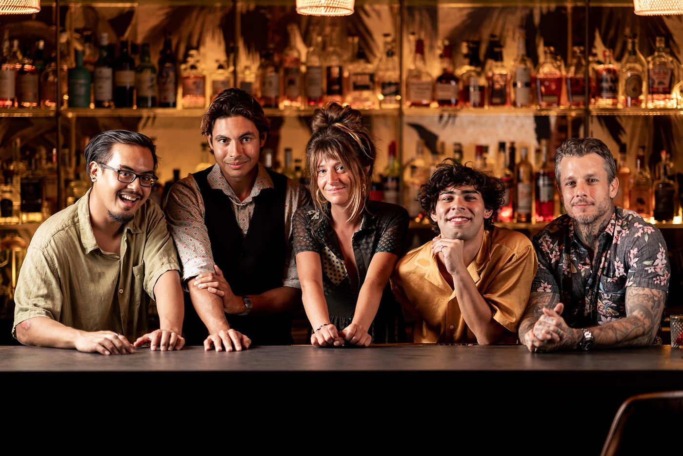 Five smiling bar staff leaning on a bar counter