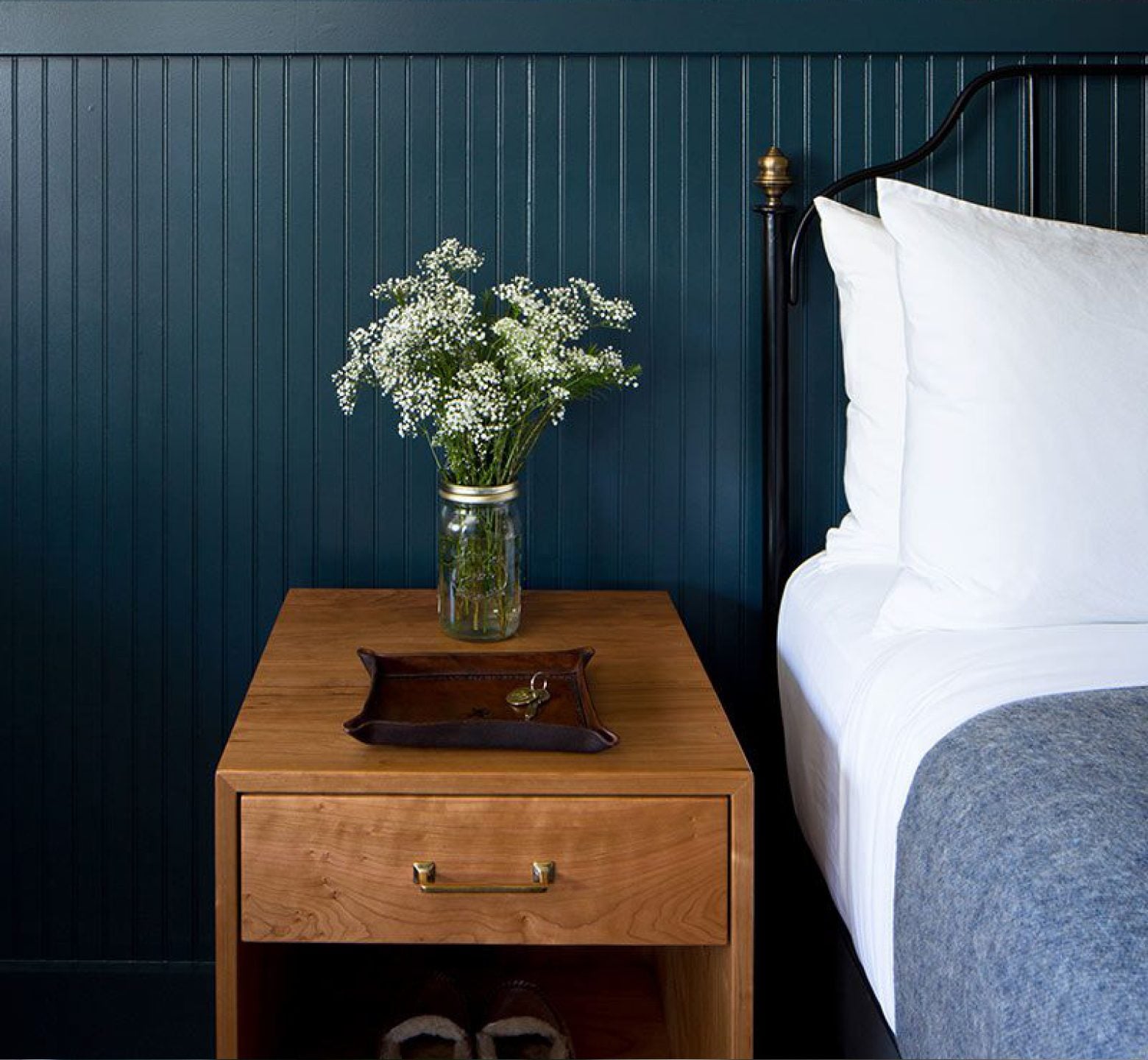 Wooden bedside table with flowers against a dark green panelled wall