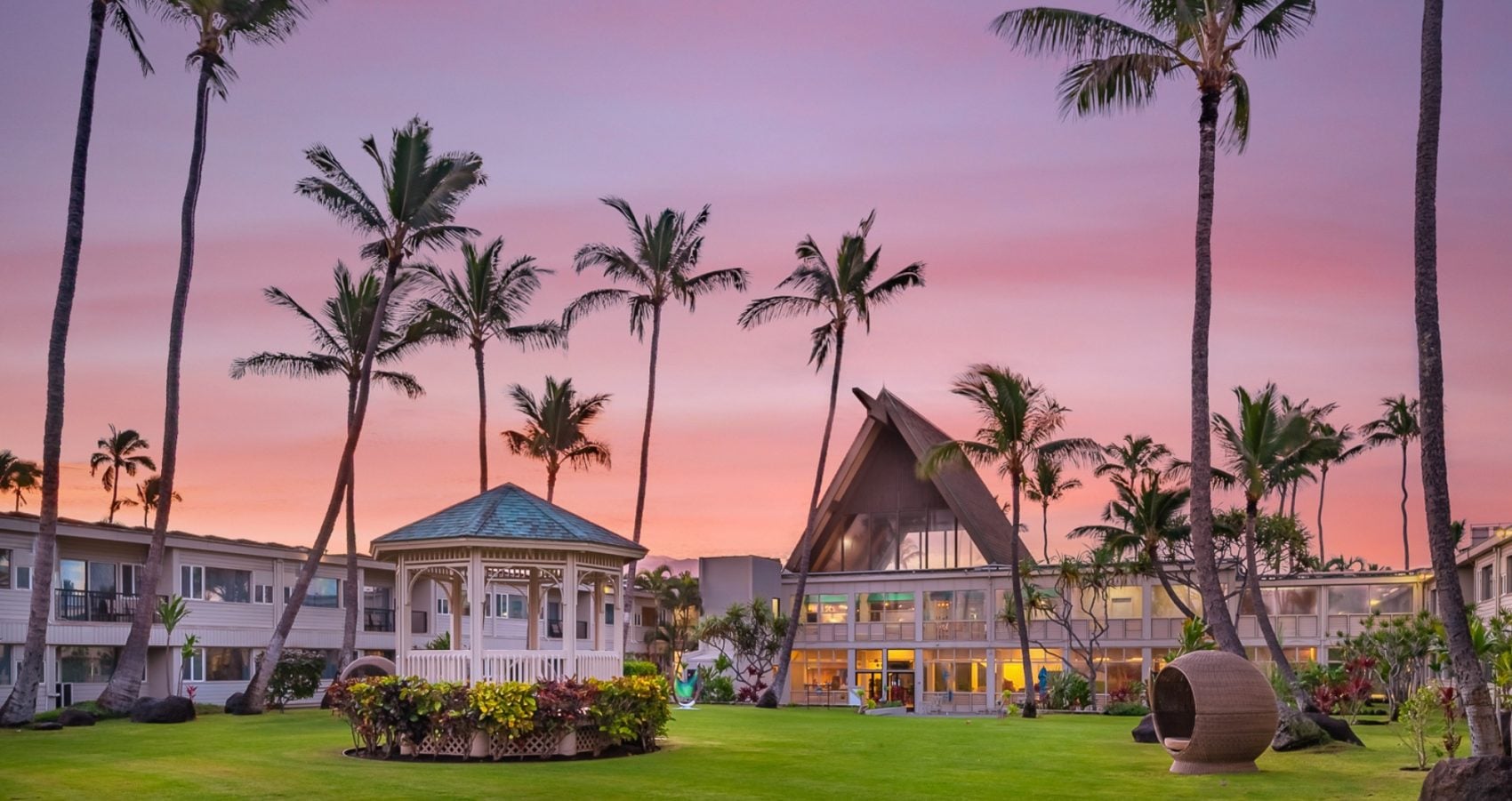 Maui resort lawn with palm trees, a gazebo, and an A-frame lodge under a pink sunset sky