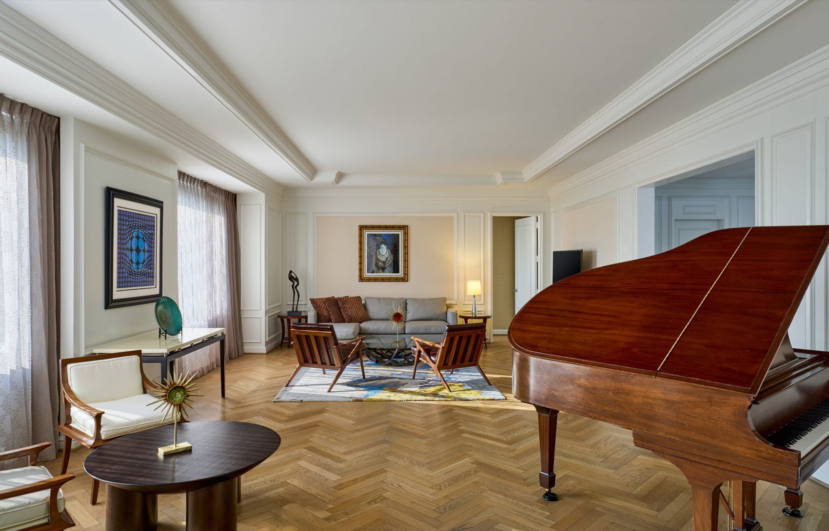 Hotel suite living room with a grand piano, herringbone wood floor, and lounge seating